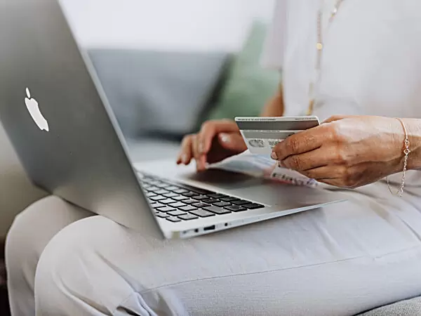 person using a macbook and holding a credit card